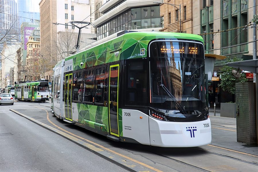 A new green and white G-class tram in the city, with an older tram behind